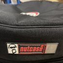 Černý textilní obal z hrubé tkaniny. Na boku je přišitý štítek s logem v podobě stylizované postavy v brýlích a nápisy „nutcase“ a „PROTECTIONrocket“…