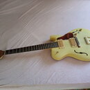Kytara typu semi-hollow s krémovým povrchem a f-otvorem. Nástroj má dva snímače s krémovými kryty, hnědý plechtr ochránič z materiálu imitující želvu…