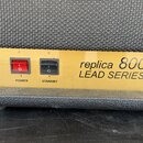 Detailní pohled na ovládací panel kytarového komba v zlaté barvě. Na panelu jsou dva přepínače s nápisy POWER a STANDBY a dva otočné knoflíky, z nich…
