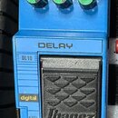 Modrý efekt pedál s nápisem DELAY a označením DL10. Na horní části jsou tři zelené otočné ovladače s popisky D-TIME, REPEAT a D-LEVEL. Na spodní část…