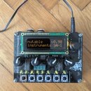 Černý elektronický modul s LCD displejem, několika otočnými knoflíky a řadou bílých tlačítek v dolní části. Na displeji je text „mutable instruments…