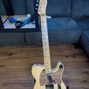 Světle žlutá elektrická kytara s tvarem typu Telecaster a javorovým hmatníkem. Na hlavě je vidět nápis "Fender" a pod ním modelové označení "TELECAST…