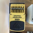 Žlutý efekt pedál s černým gumovým podložníkem. Na zařízení jsou nápisy GRAPHIC EQUALIZER, EQ700 a logo behringer. Horní část obsahuje posuvníky s oz…