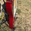 Detailní pohled na elektrickou kytaru s červeným metalizovaným lakem. Nástroj má světlý javorový hmatník a bílý pickguard. Kytara je umístěna v černé…