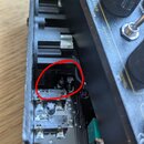 Detailní pohled do otevřeného černého šasi elektronického zařízení s viditelnou základní deskou a zapájkami. Červený kruh označuje oblast s několika…