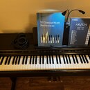 Černý digitální piano s bílými a černými klávesami. Na horní desce je nápis YAMAHA, vedle něj jsou umístěna černá sluchátka a dvě notové knihy značky…