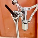 Detail chromovaného mechanismu stojanu s černou plastovou utahovací pákou. Konstrukce obsahuje kovové klouby, šrouby a vertikální trubku s zakončením…