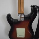Zadní strana elektrické kytary s barevným přechodem od černé přes červenou k žluté. Na kovovém spojovacímdesce krku je logo Fender a nápisy PLAYER ST…