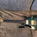 Elektrická kytara s modro-černým přechodovým lakem a krčkem z tmavého dřeva. Na hlavě je viditelné logo Ibanez a nápis RG SERIES. Nástroj má dva humb…