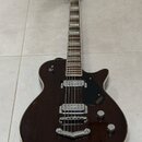 Tmavně hnědá elektrická kytara s polodupovým tělem a bílým lemováním. Na černém plechtraci je viditelné logo GRETSCH a nápis Broadkaster. Nástroj má…