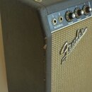 Detail kytarového komba s černým texturovaným potahem a béžovou textilní maskou. Na masce je umístěno kovové logo Fender. Ovládací panel obsahuje náp…