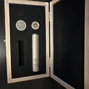 V dřevěném kufru s černou pěnovou výplní je umístěn stříbrný kondenzátorový mikrofon. Na těle mikrofonu je svislý nápis „Made in Russia Tula“ následo…