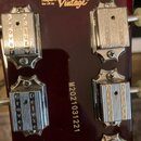 Záběr na tmavě červenou hlavu kytary s chromovanými ladicími kolíky. V horní části je nápis „Vintage a John Hornby Skewes Product®“ a pod ním logo „V…
