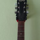 Fotografie zachycuje hlavu a hmatník elektrické kytary v černé barvě. Na horní části hlavy je bílý nápis Epiphone a na zadní straně v dolní části svi…