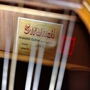 Detail vnitřku akustické kytary s papírovým štítkem. Na štítku je červený nápis Strunal, text Acoustic Guitar Made in Luby, Czech Republic a u pole m…