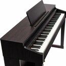 Digitální piano v tmavě hnědé barvě s povrchem imitujícím dřevo. Nástroj má bílé a černé klávesy a přiložený jednoduchý notový pult. Na viditelných č…