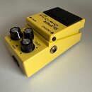 Žlutý efekt pedál s černým spínacím tlačítkem. Na horní části je nápis SUPER OverDrive SD-1 a šipky s označením INPUT a OUTPUT. Na boku jsou tři čern…