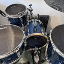 Sada modrých bubnů s kovovým kováním. Na blanách jsou viditelné nápisy EVANS a RTOM MESH HEAD. Na pedálu je nápis IRON COBRA. Povrchy nástrojů vykazu…