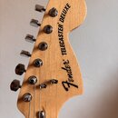 Hlava elektrické kytary z přírodního světlého dřeva s chromovanými ladičkami. Na povrchu je černý nápis Fender TELECASTER DELUXE. Povrch dřeva a kovo…