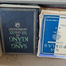 Kartonová krabice s několika knihami a sešity. V popředí jsou dvě knihy, z nichž levá má tmavomodrý krycí papír se zlatým rámečkem a nápisem SANG UND…