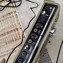Zadní panel hudebního přístroje v šedobéznaté barvě s černým polem konektorů. V horní části je sekce INPUTS s konektory a nápisy AUX IN, COMPS IN. Sp…