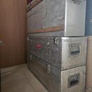 Dvě stohované transportní bedny z hliníku. Horní bedna má dřevěné lišty a viditelné opotřebení povrchu v podobě škrábanců a odirení. Spodní bedna je…