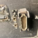 Detailní pohled na černý transportní case s několika konektory a úchytkou. Na šedém vícepinovém konektoru je viditelné logo HARTING. Vedle něj se nac…