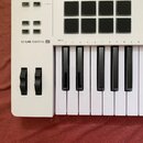 Bílá MIDI klaviatura s černými klávesami a ovládacími prvky. Na levé straně je nápis KEYLAB ESSENTIAL 49 a několik tlačítek s popisky MIDI Ch, Bank,…