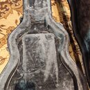 Otevřený tvrdý kufýr na kytaru s šedým plyšovým vnitřkem. Na levé straně krku je vidět nápis „Gibson“. Povrch vnitřního polstrování vykazuje známky o…