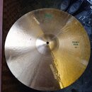 Zlatavý mosazný činel s viditelným kovánívým povrchem. Na povrchu jsou nápisy „Meinl“, „HEAVY RIDE 20“ a nečitelný text v blízkosti středu. Povrch vy…