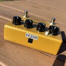 Zlatý efekt pedál s čtyřmi černými otočnými knoflíky a dvěma stříbrnými spínači. Na horní straně je nápis "sub octave bass fuzz" a nečitelné logo. Na…