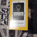 Žlutá krabice s obrázkem efekt pedálu. Na černém panelu pedálu jsou nápisy LPB-1, LINEAR POWER BOOSTER a BOOST, v dolní části je text Electro-harmoni…
