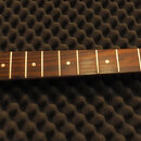 Hmatník elektrické kytary z tmavého dřeva s bílými polohovými značkami. Světle žlutá hlava kytary nese nápisy Squier a STRATOCASTER, v dolní části je…