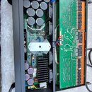 Fotografie ukazuje vnitřek černého kovového šasi s elektronickými komponenty. Vevnitř jsou umístěny dvě zelené základní desky s osazením kondenzátorů…