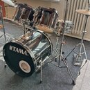 Černá bicí souprava s kovovým hardwarem. Na předním bendle basového bubnu je bílý nápis TAMA a vlevo svisle menší nápis Starclassic. Souprava obsahuj…