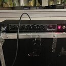 Černý rackový efekt s nápisem SansAmp TECH 21. Na předním panelu se nachází řada ovládacích knoflíků s popisky INPUT, DRIVE, PRESENCE, BLEND, BASS, M…