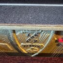Detailní záběr na zlatý kovový štítek s logem výrobce vložený do nástroje. Na štítku je vyražen nápis PETROF a nad ním písmeno P. Povrch štítku vykaz…