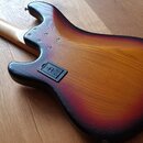 Zadní strana elektrické kytary s tělem z dřeva v červeno-žlutém přechodovém odstínu (sunburst). Na těle je vidět černý kryt vložky krku s nečitelným…