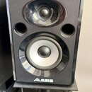 Černý studiový monitor s lesklým povrchem, umístěný na černém stojanu. Na přední straně jsou dva reproduktory a dva kruhové odvětrávací otvory. V dol…