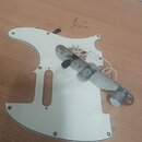 Bílá pickguard z plastu s vyřezanými otvory pro snímače a ovládací prvky. Na pickguard je připevněn kovový most s dvěma cylindrickými saddles a černý…