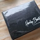 Černá kartonová krabice s nápisy bílou barvou. Na povrchu je vidět logo „Harley Benton“ a pod ním text „CUSTOM LINE PEDAL“. Povrch krabice vykazuje m…