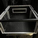 Otevřený černý transportní case s hliníkovými hranami a profilemi. Vnitřní prostor je prázdný, v zadní stěně je umístěn obdélníkový výřez s hliníkový…