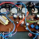 Fotografie zachycuje vnitřek šedého plastového boxu s elektronickým obvodem na hnědé perforované desce. Na horní části jsou umístěny tři kovové součá…