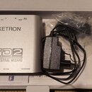Stříbrný efektový pedál s nápisy KETRON, SD2 a ORCHESTRAL WIZARD. Na horní hraně jsou označení vstupů: POWER DC 12V, L OUT, R OUT, IN MIDI a THRU MID…