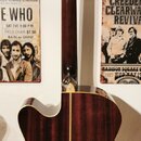 Zadní pohled na akustickou kytaru s tmavě hnědým dřevěným povrchem a výraznou sletovanou strukturou. Na hlavě hmatníku je nápis „Eastman Guitar Compa…