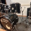 Černá bicí souprava s chromovaným kováním, sestávající z basového bubnu a dvou tomů. Na přední blaně basového bubnu jsou bílé nápisy SONOR a SHURE, v…