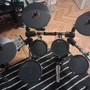 Elektronická bicí souprava s černými padovými plochami a činely. Na několika pádech a na horní příčce rámu je viditelný nápis CARLSBRO. Souprava obsa…