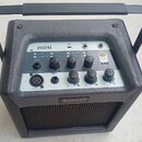 Černý přenosný kombozesilovač s rukojetí. Na horním ovládacím panelu je nápis mini a pod ním řada přepínačů s popisky NATURAL, TWIN REVERB, PARLOR, S…