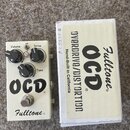 Bílý kytarový efekt s nápisy OCD a Fulltone®. Na horní části jsou tři černé ovládací knoflíky s popisky Volume, Drive a Tone a přepínač HP/LP. Vedle…