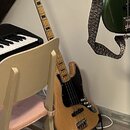Na fotografii je čtyřstrunná basová kytara s přírodním dřevěným povrchem těla a hmatníku. Tělo má černý pickguard a čtyři ladicí kolíky na hlavě. Nás…